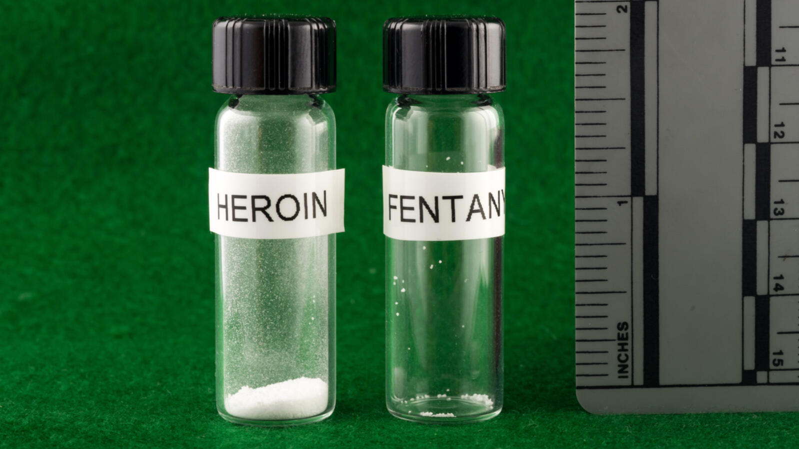 A vial labelled "heroin" holding a considerable amount of powder and a vial labelled "fentanyl" with a few grains of powder.
